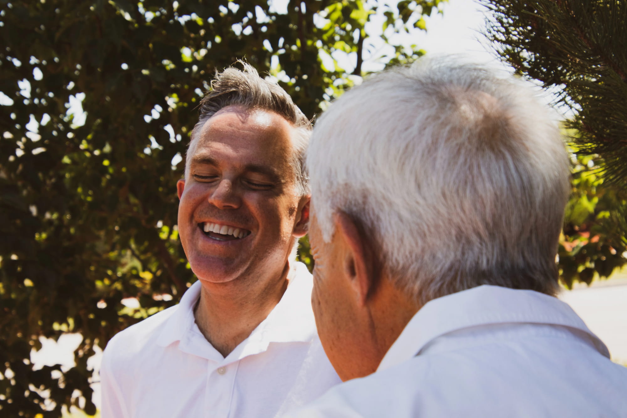 An elderly father and middle-age son laughing together outside.