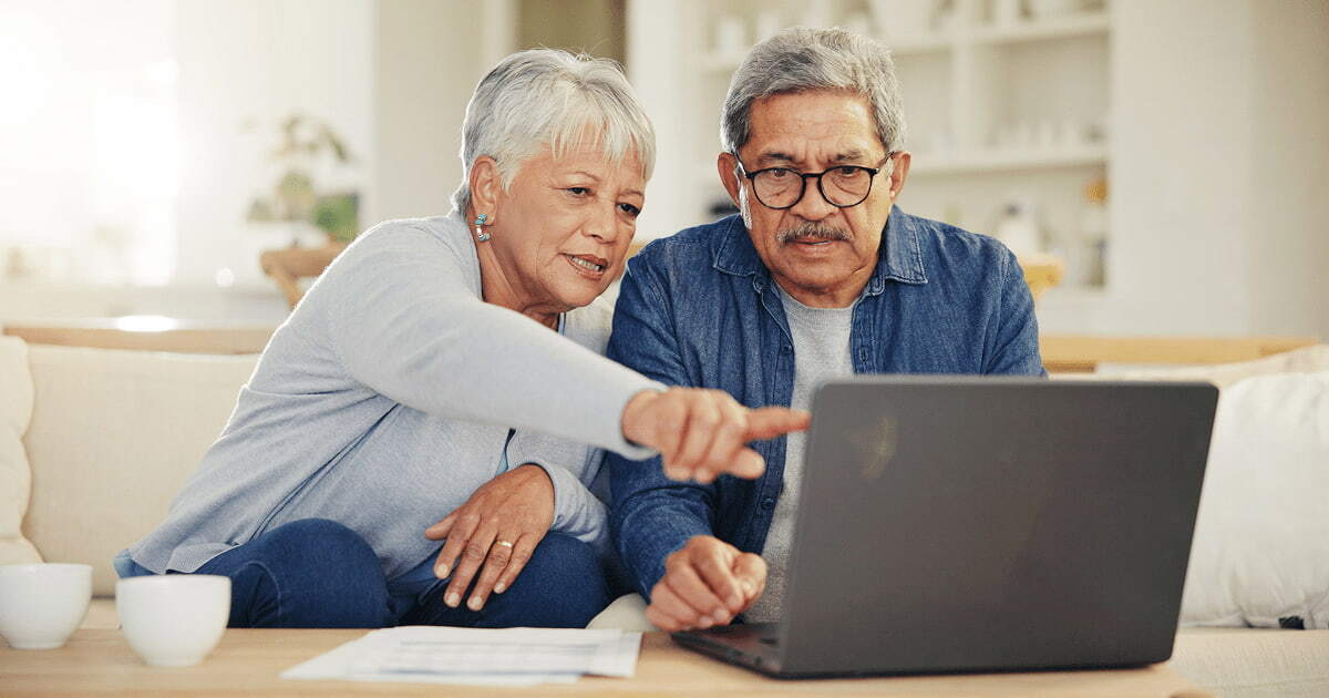 A retired couple sits together looking over a laptop.